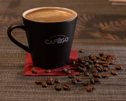 Cafego coffee mug filled with espresso surrounded by coffee beans on textured surface.