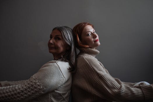 Two women sitting back to back in cozy sweaters, symbolizing connection and intimacy.