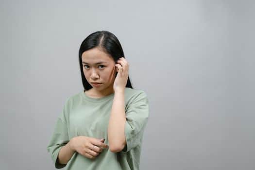 Thoughtful woman in green top appears shy with a subtle expression against a plain studio backdrop.