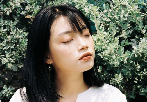 Peaceful portrait of a young woman basking in sunlight amidst greenery in Ho Chi Minh City.
